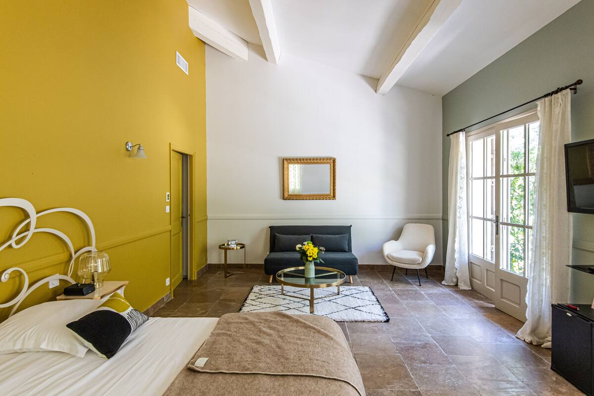 Une chambre d’hôtel avec un lit, un canapé, une table basse, une télévision et une fenêtre avec des rideaux.