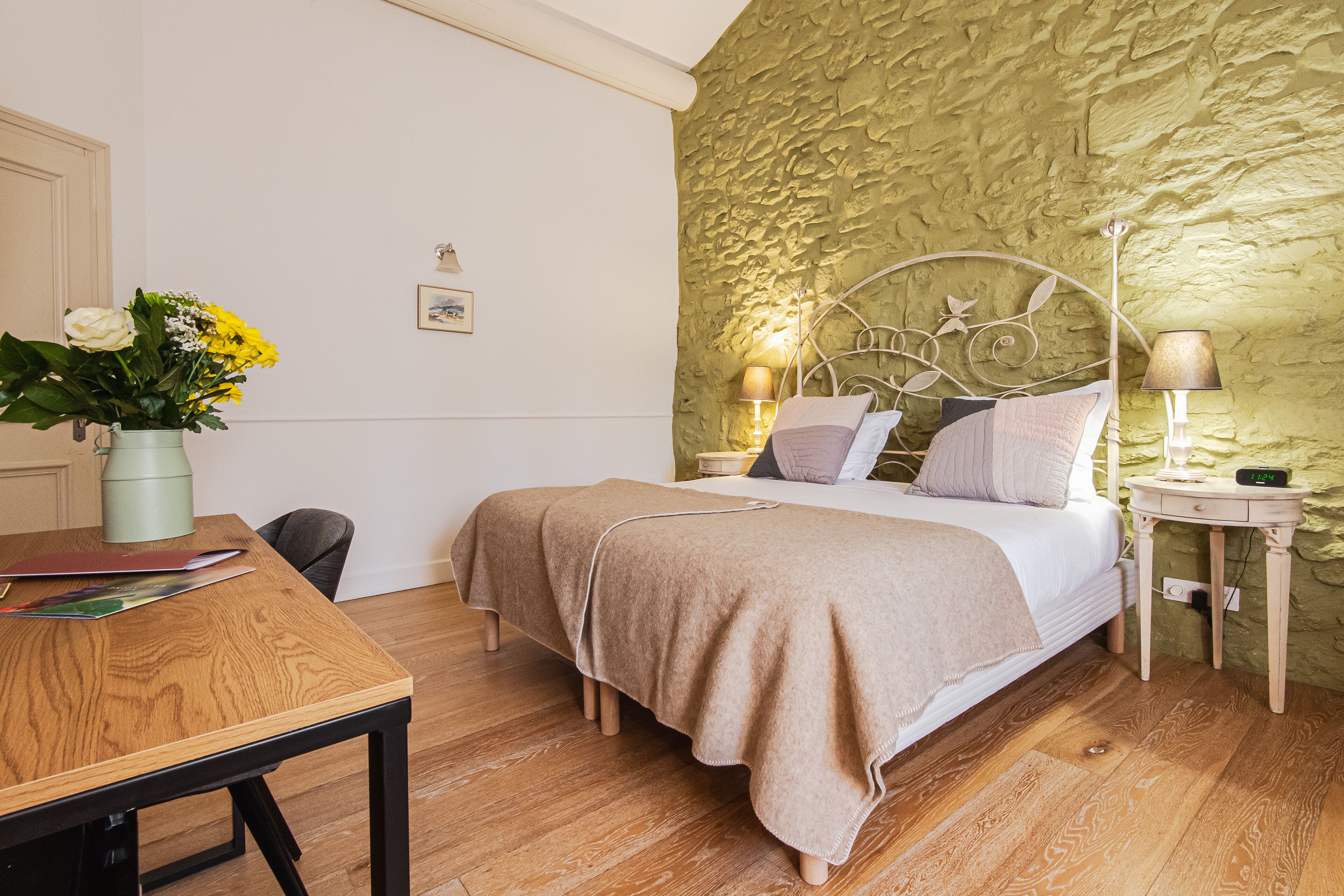 A bedroom with a bed, bedside tables, a lamp, and a desk with a vase of flowers.