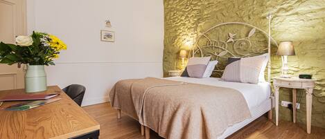 A bedroom with a bed, bedside tables, a lamp, and a desk with a vase of flowers.