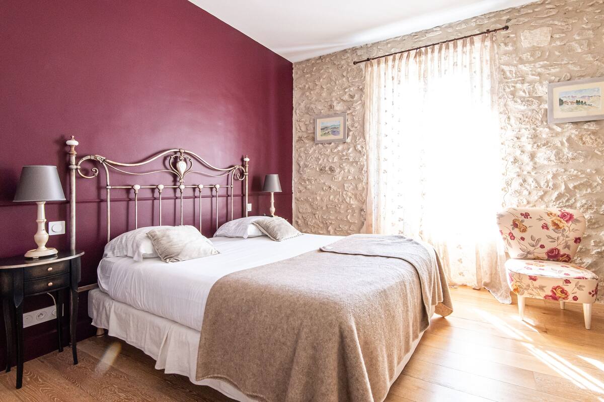 Une chambre à coucher avec un lit, deux tables de chevet, une chaise et un mur en pierre.