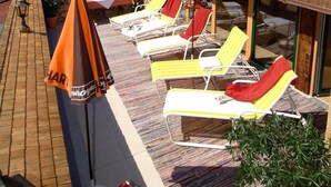 A terrace with sun loungers, a table, and a potted plant. - Hotel Sportalm (Gerlos)