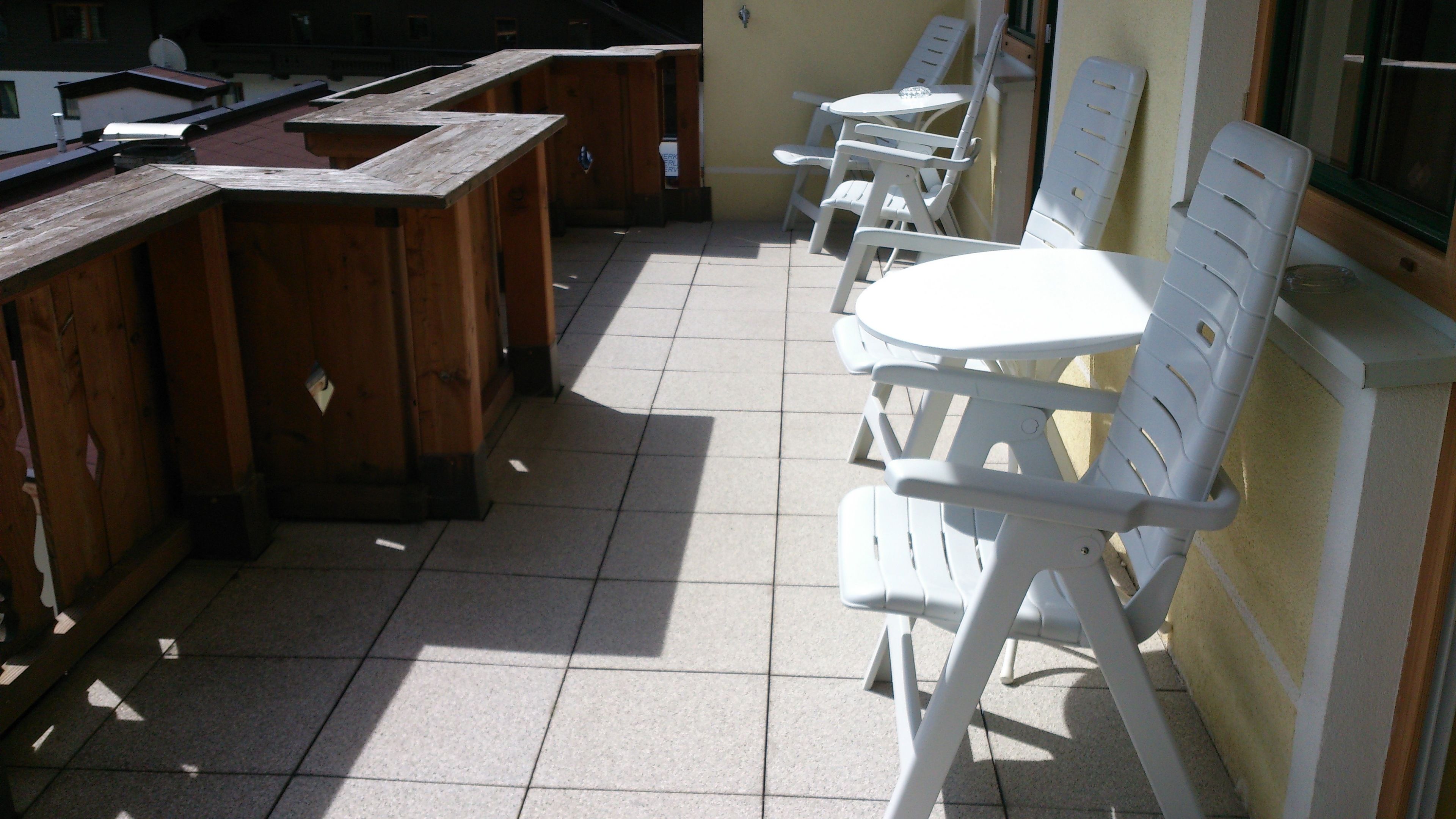 A patio area with wooden tables and white plastic chairs.