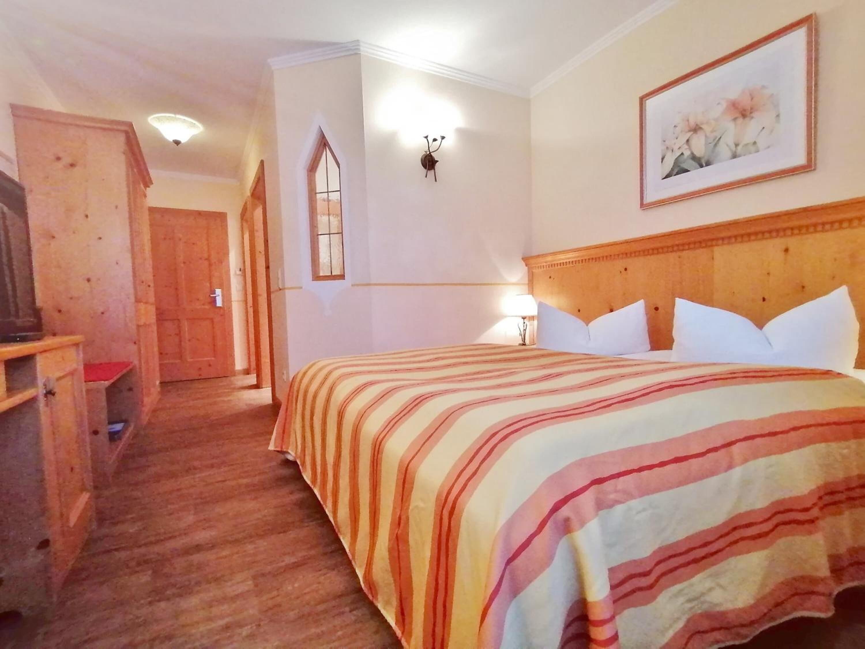 Quarto de hotel com cama de madeira, mesa de cabeceira, escrivaninha e janela com vista.