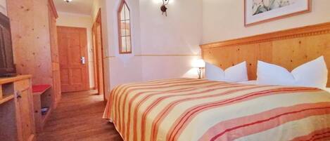 Quarto de hotel com cama de madeira, mesa de cabeceira, escrivaninha e janela com vista.