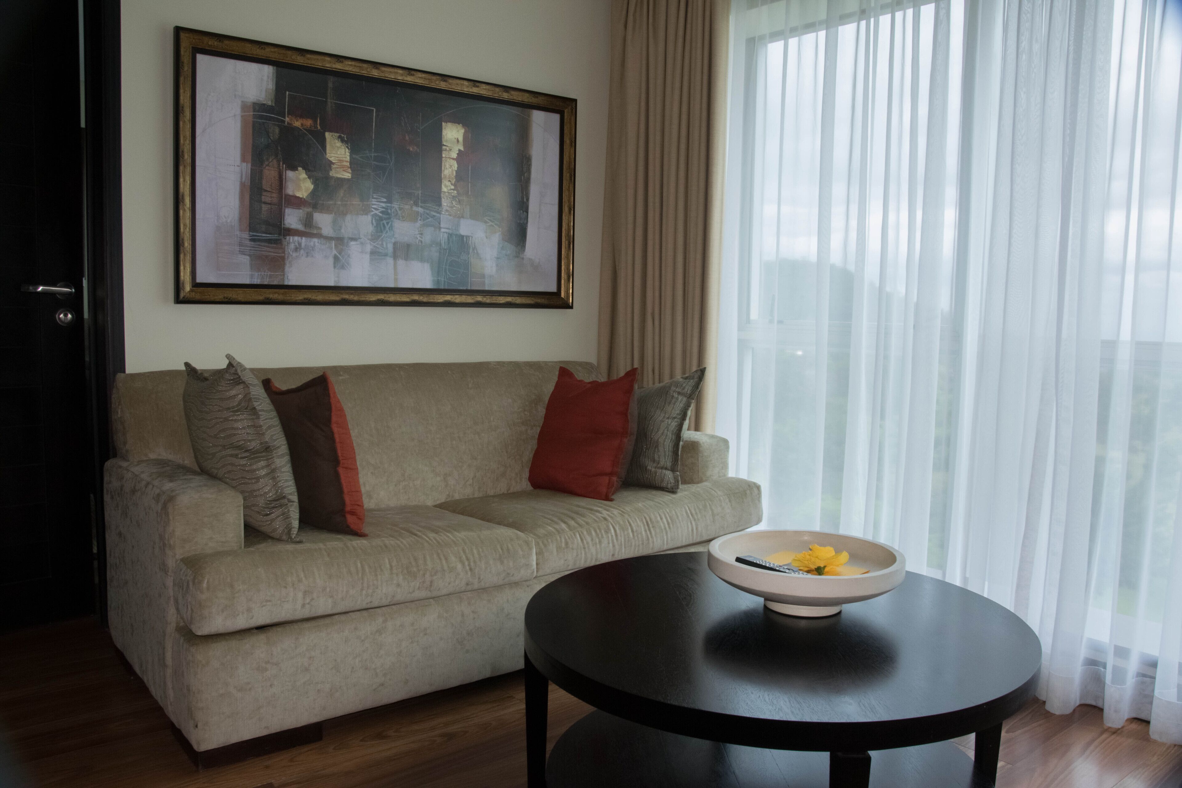 A living room with a beige sofa, a black coffee table, and a framed abstract painting on the wall.