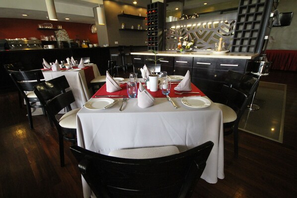 Un restaurante con mesas dispuestas para comer, sillas y una zona de bar al fondo.