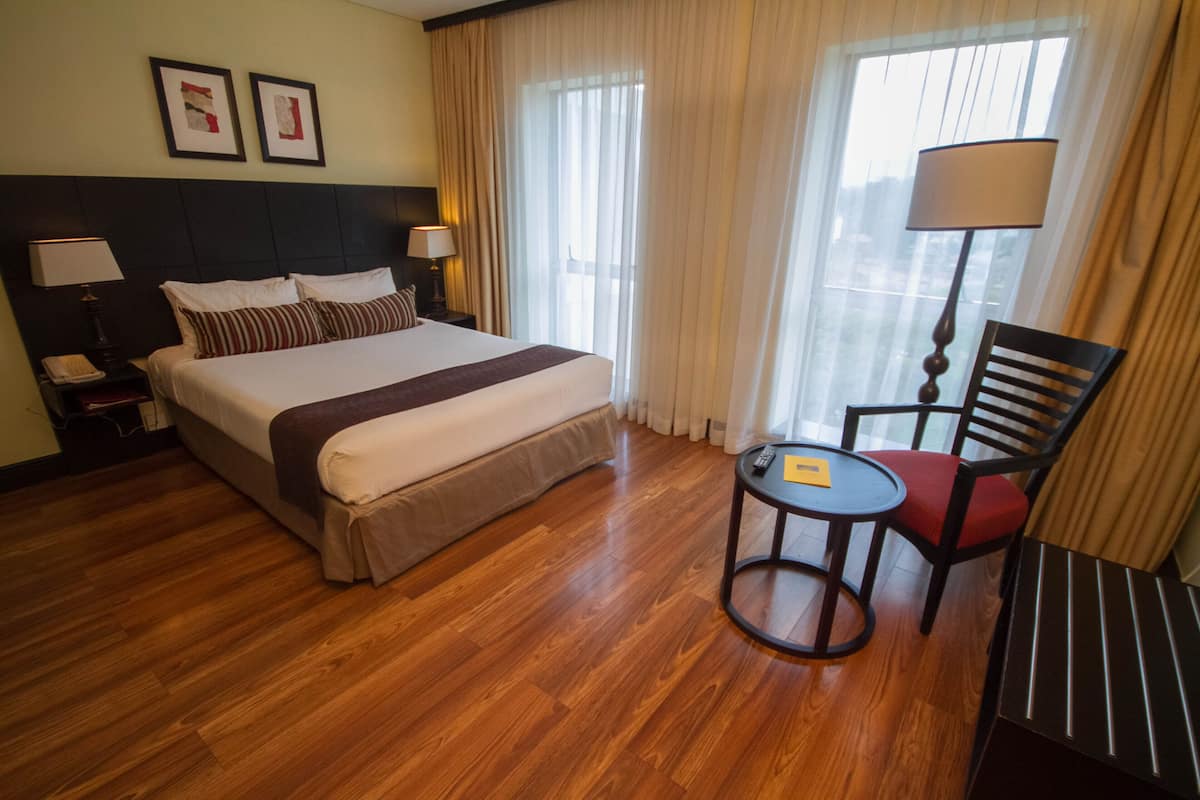 Habitación de hotel con una cama grande, una mesita de noche con lámpara, una silla y una pequeña mesa con control remoto.