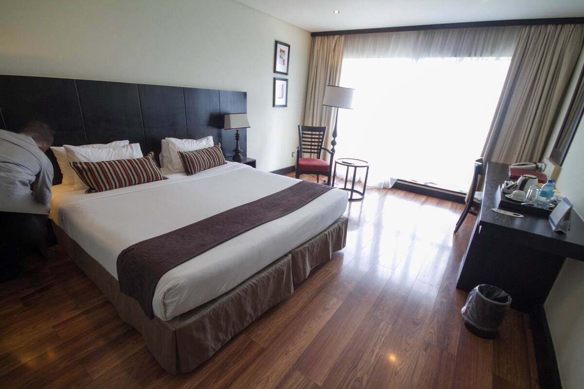 Habitación de hotel con una cama grande, un escritorio con lámpara, una silla y vistas al exterior.