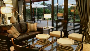 A modern lounge area with leather sofas, round tables, and chairs, featuring large windows and outdoor umbrellas. - Mount Meru Hotel (Arusha)