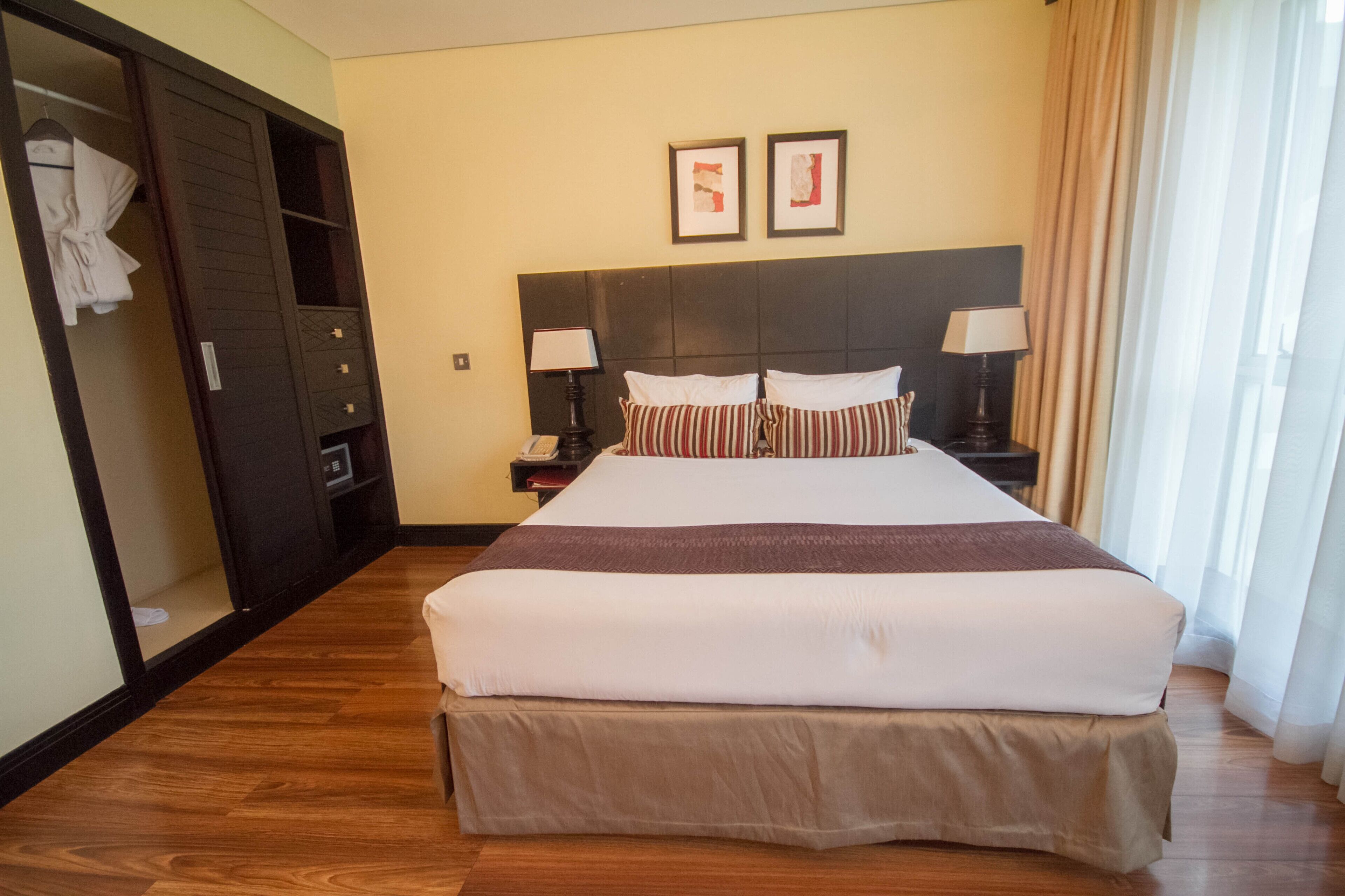 A hotel room with a large bed, two bedside tables with lamps, a wardrobe, and two framed pictures on the wall.