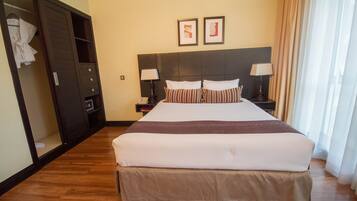A hotel room with a large bed, two bedside tables with lamps, a wardrobe, and two framed pictures on the wall.