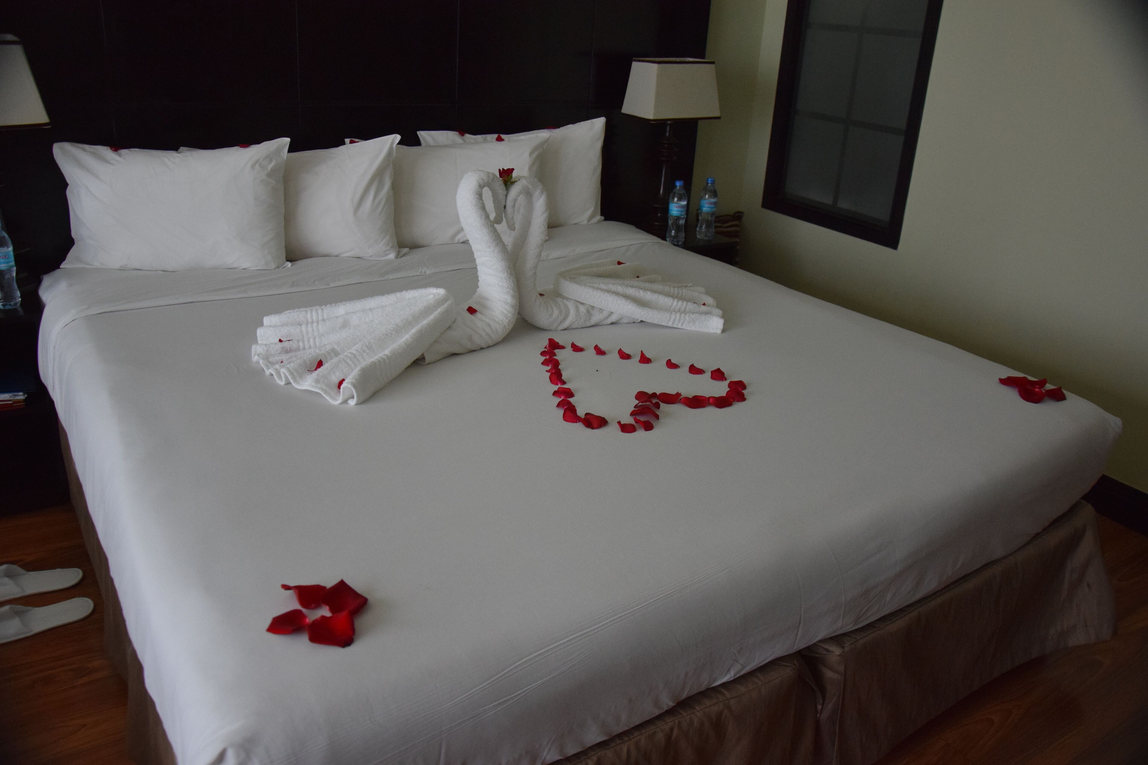 Un letto rifatto con lenzuola bianche, un'armatura a forma di cuore di petali di rosa e due asciugamani piegati a forma di cigno.