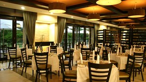 A restaurant with multiple tables and chairs, large windows, and hanging pendant lights. - Mount Meru Hotel (Arusha)