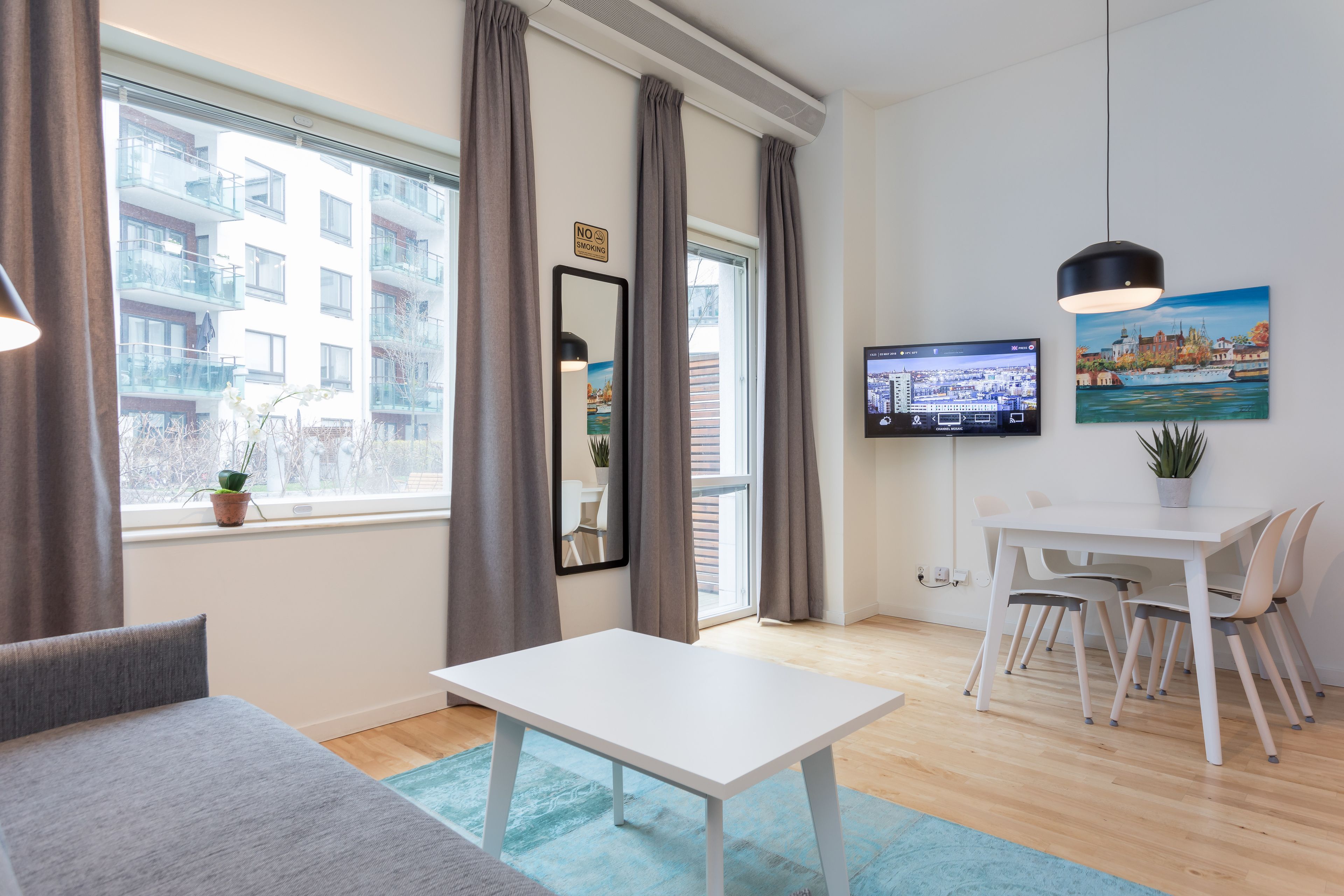 Une chambre d’hôtel moderne dotée d’une grande fenêtre, d’un coin repas avec une table et des chaises, d’un téléviseur à écran plat fixé au mur et d’une plante en pot posée sur le rebord de la fenêtre.