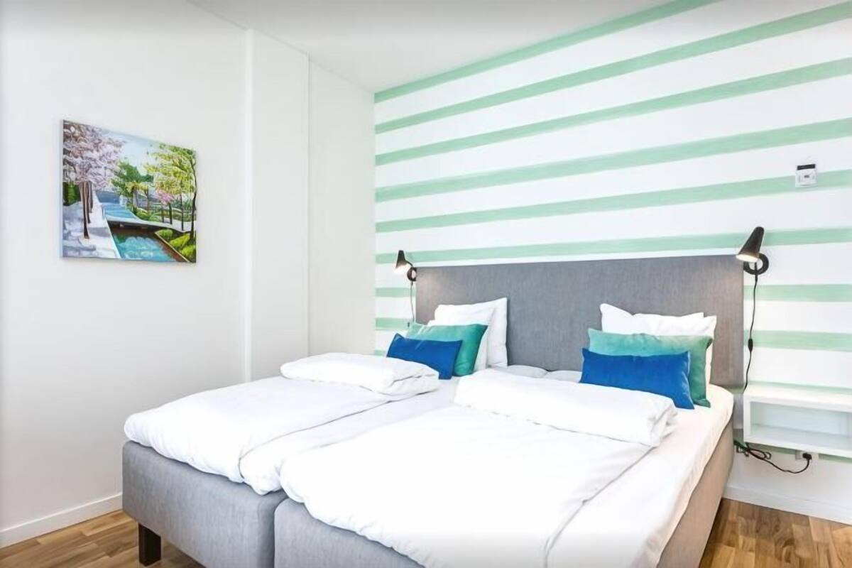 A double bed with white and blue bedding, a headboard, and a wall-mounted lamp.