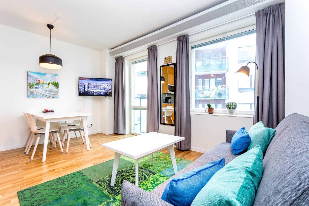 A modern living room with a white table, grey sofa, and a green patterned rug.
