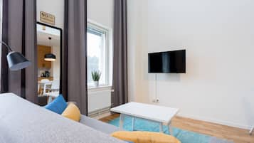 Sala de estar moderna com sofá, uma mesa pequena, televisão e vista para uma cozinha através de um espelho.