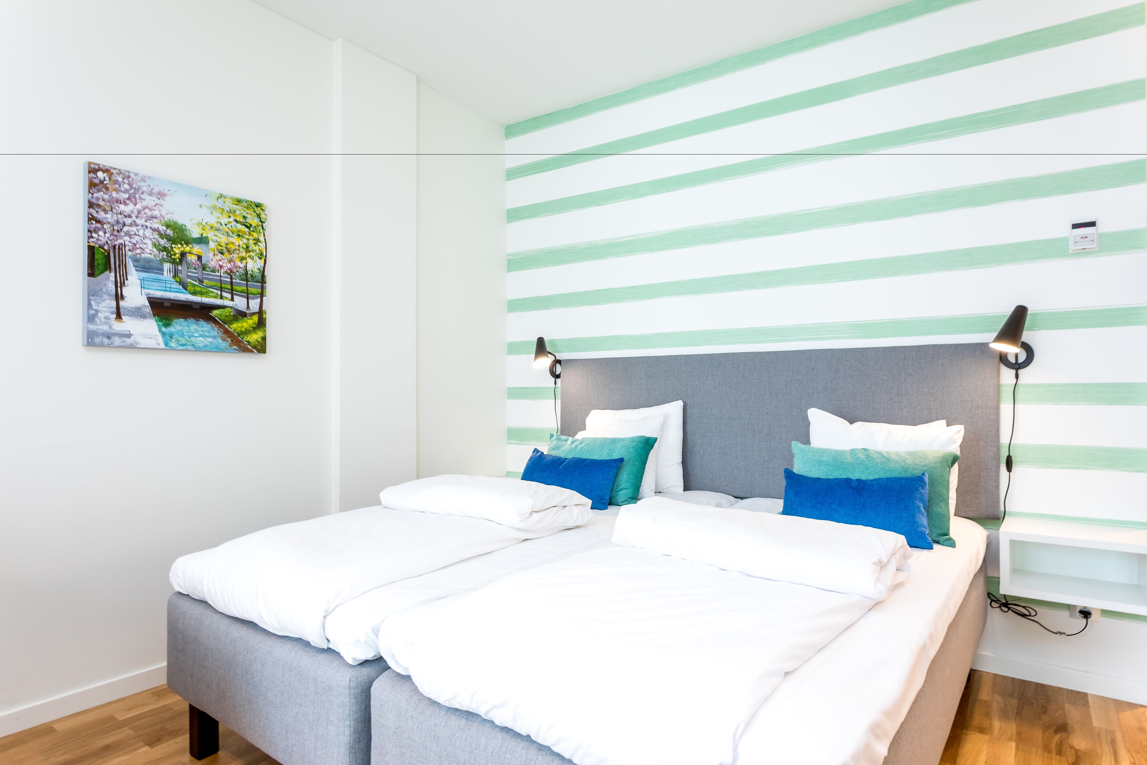 Een moderne slaapkamer met een bed, kussens, een hoofdbord, een schilderij en een gestreept behang.