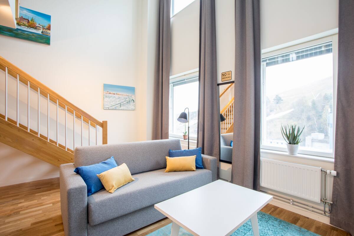 A modern living room with a grey sofa, a white coffee table, and a staircase.