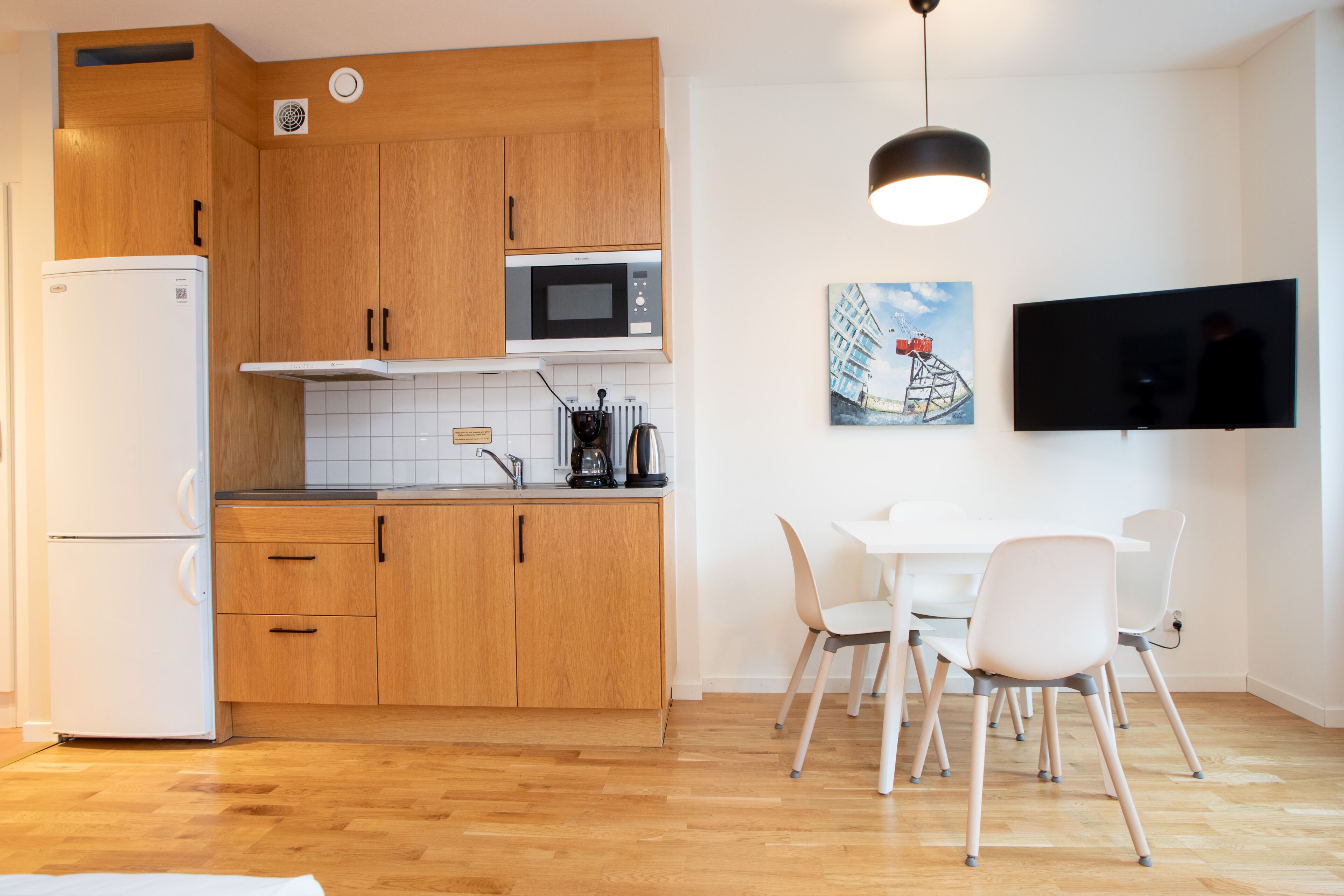 A modern kitchen with wooden cabinets, a microwave, and a dining area with white chairs and a table.
