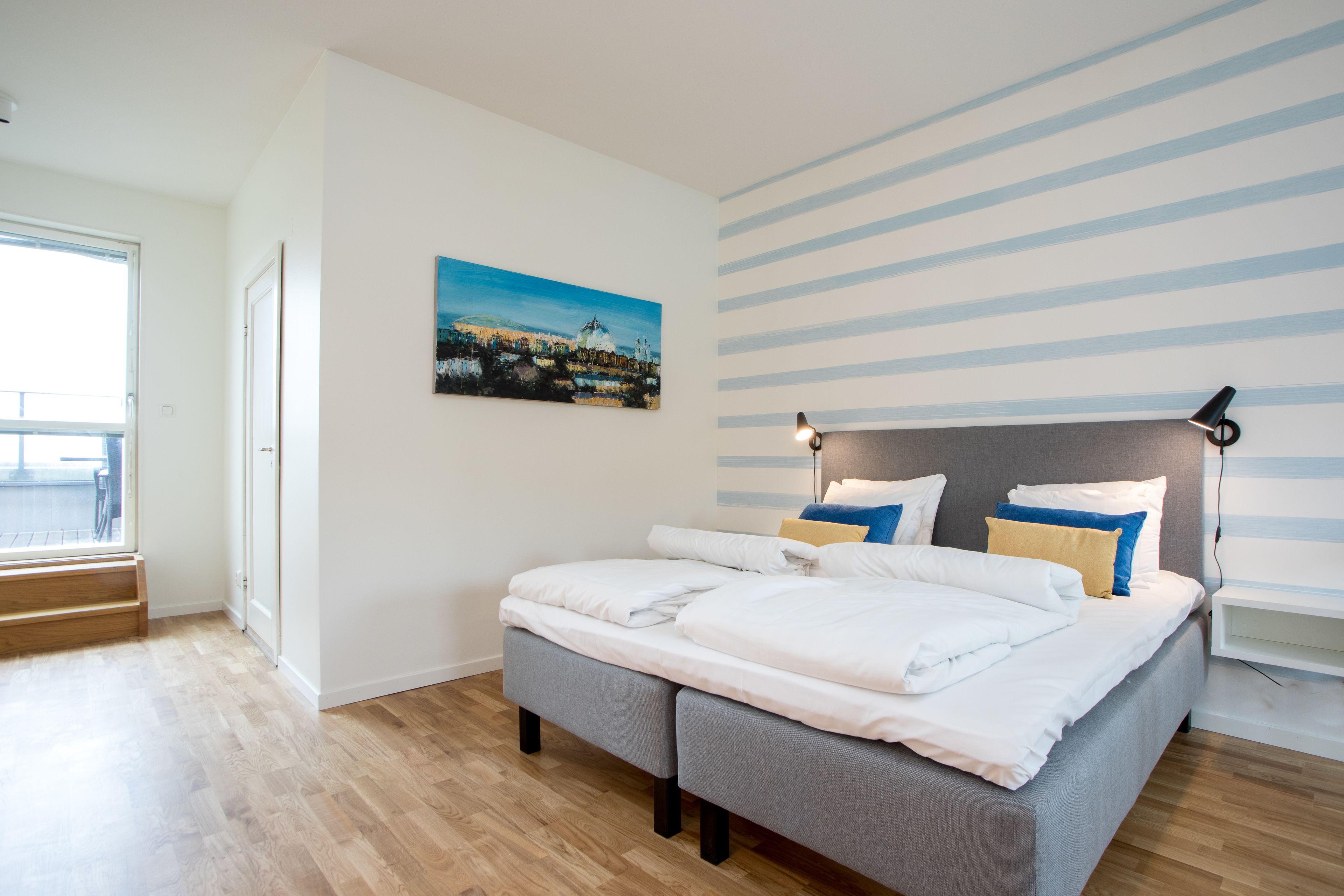 A modern bedroom with a bed, a painting, a striped wall, and a window.