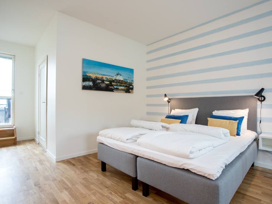 Ein modernes Schlafzimmer mit einem Bett, einem Gemälde, einer gestreiften Wand und einem Fenster.