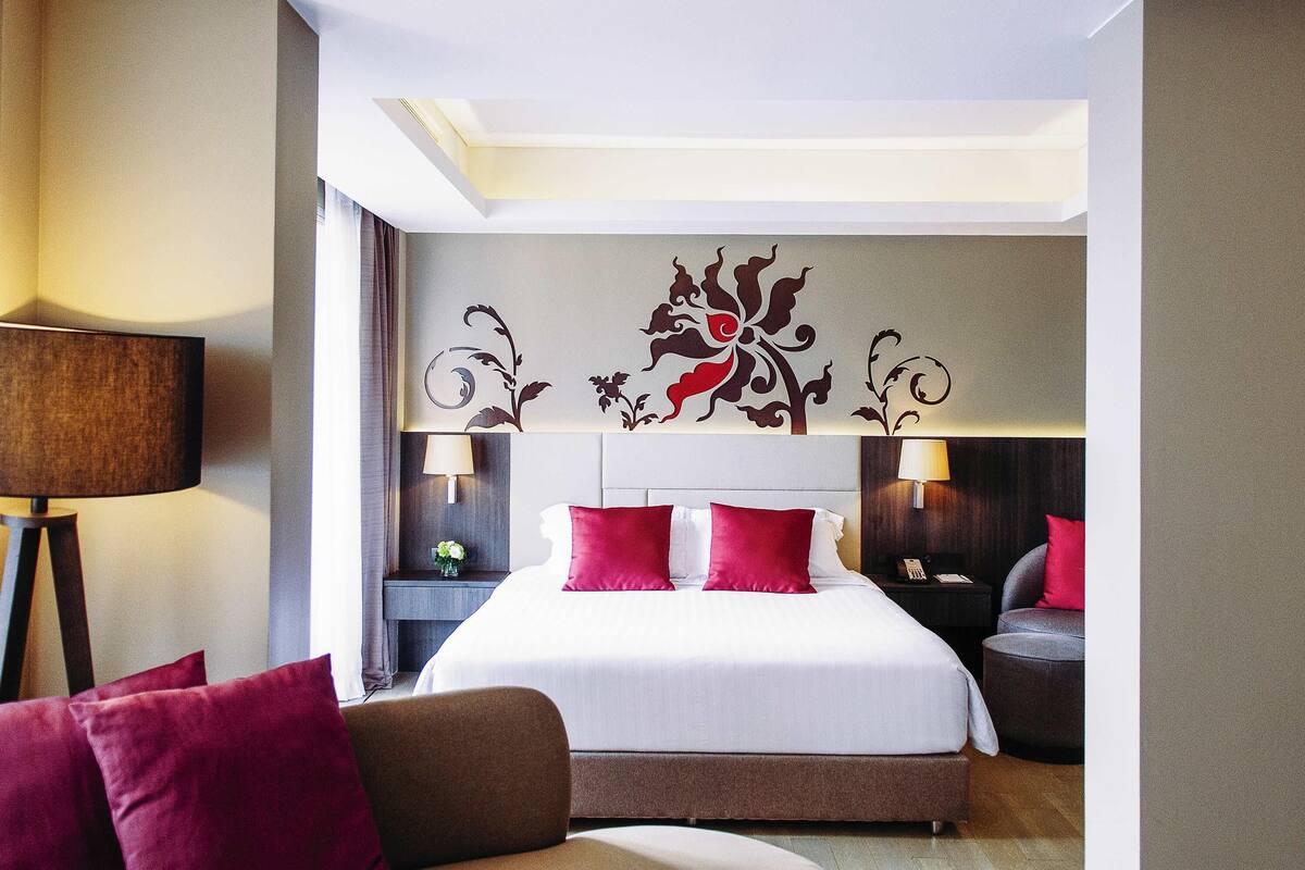 Une chambre d’hôtel avec un grand lit, deux tables de chevet avec des lampes, un canapé et une fresque murale décorative.