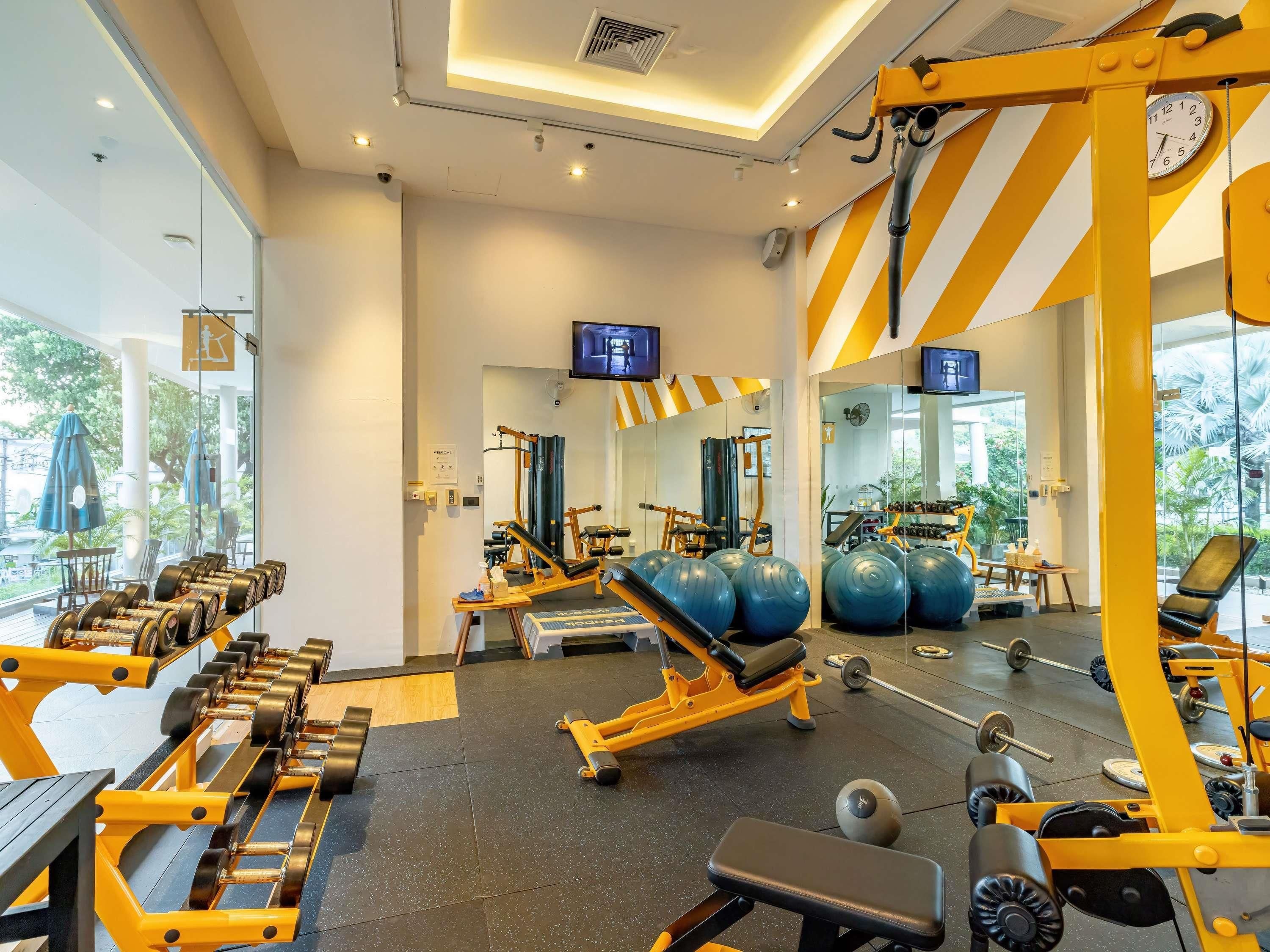 Un gimnasio con equipo de ejercicio, espejos y un reloj.