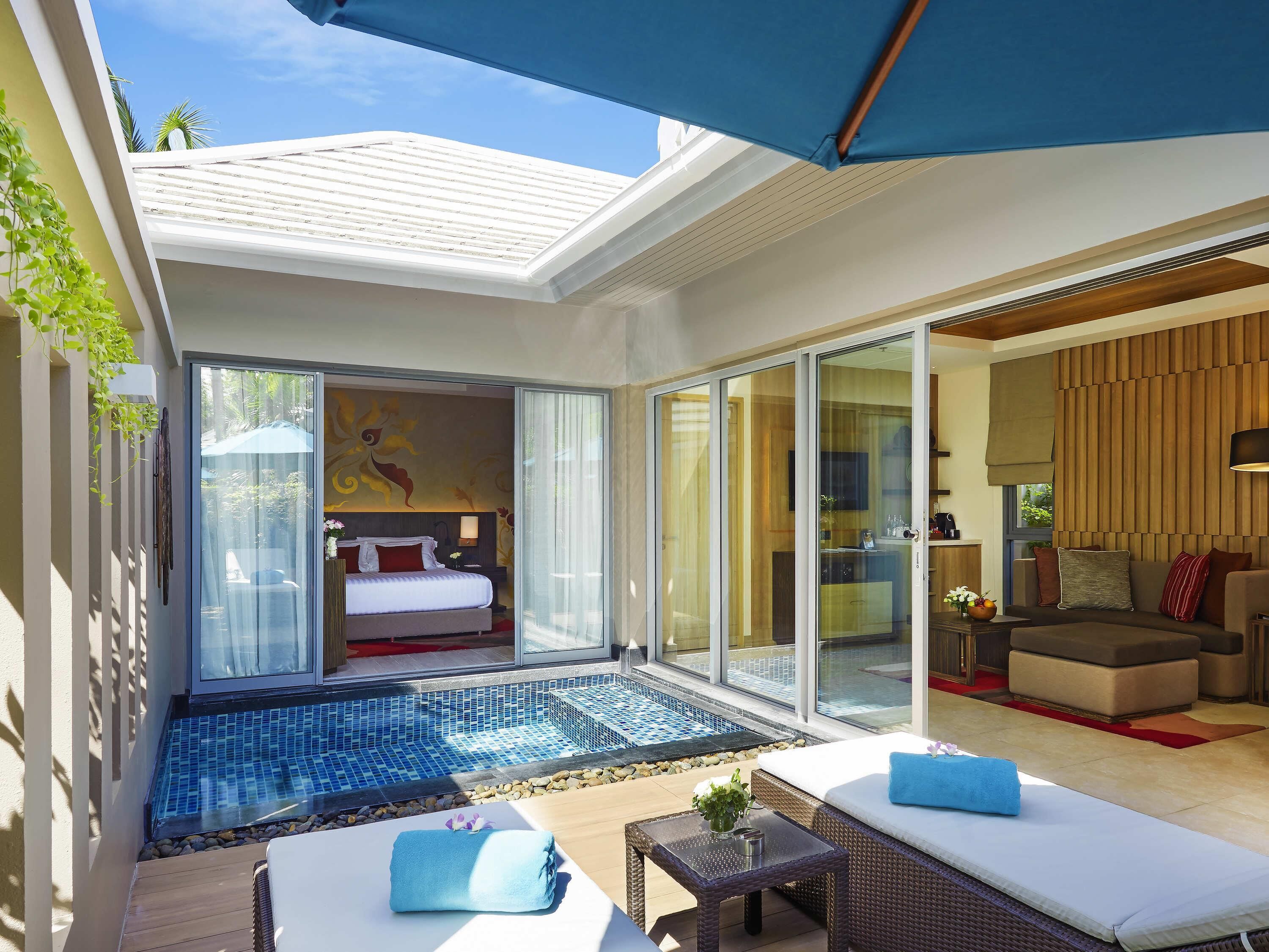 Ein modernes Hotelzimmer mit Glastür zu einem Balkon, einem Pool und einem Wohnbereich mit Sofa und Tisch.