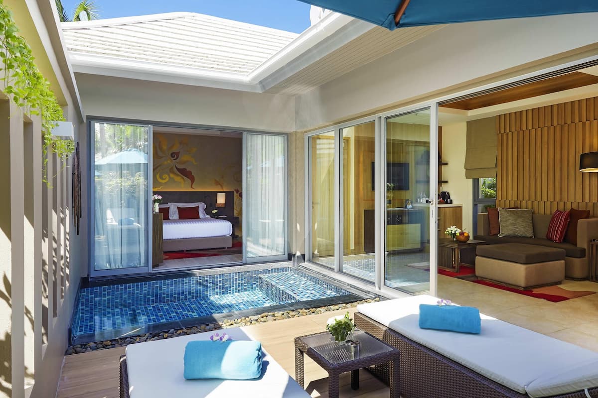 Une chambre d’hôtel moderne dotée d’une porte vitrée donnant sur un balcon, une piscine et un espace de vie avec un canapé et une table.