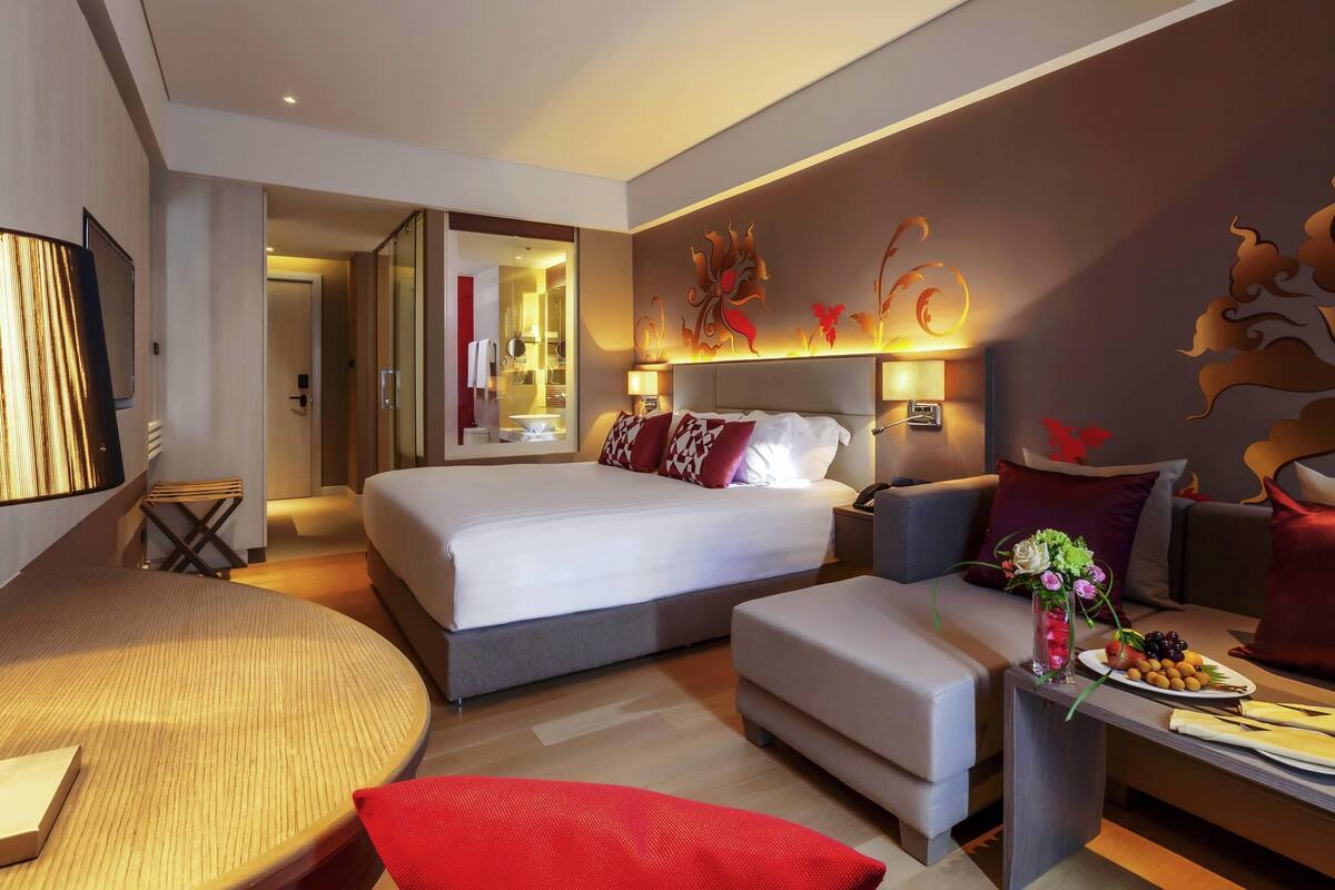 Une chambre d’hôtel moderne dotée d’un grand lit, d’un coin salon avec une table ronde et d’une petite kitchenette.