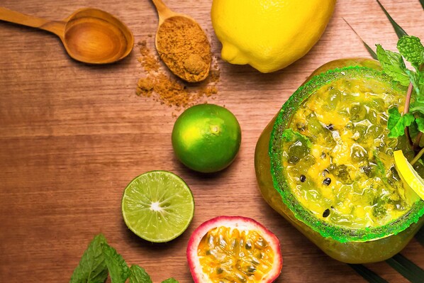 A wooden surface with a lime, a halved lime, a spoon with a powdery substance, a whole lemon, and a halved passion fruit with a green rind.