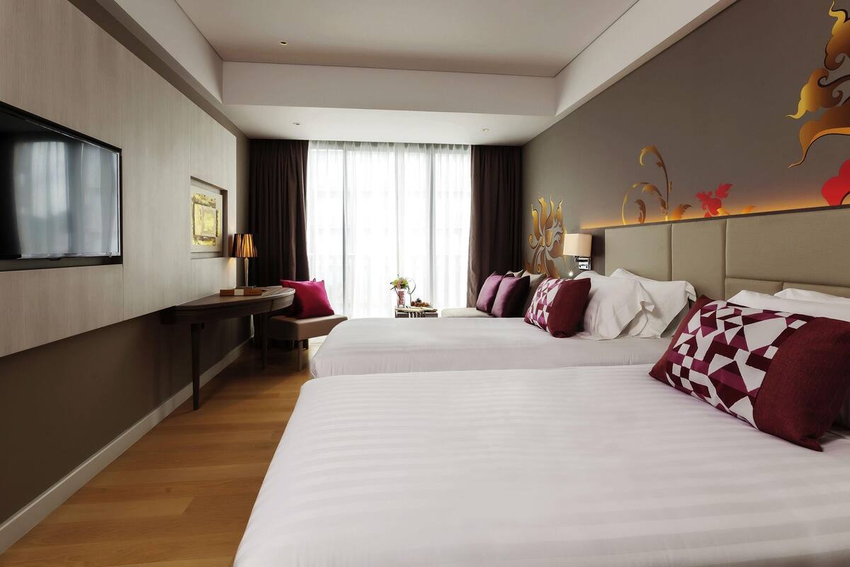 Une chambre d’hôtel avec deux lits, un bureau, une télévision et une grande fenêtre avec des rideaux.