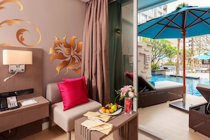 Hotelkamer met een bank, een kleine tafel met een schaal fruit, een vaas met bloemen en uitzicht op een buitenzwembad.