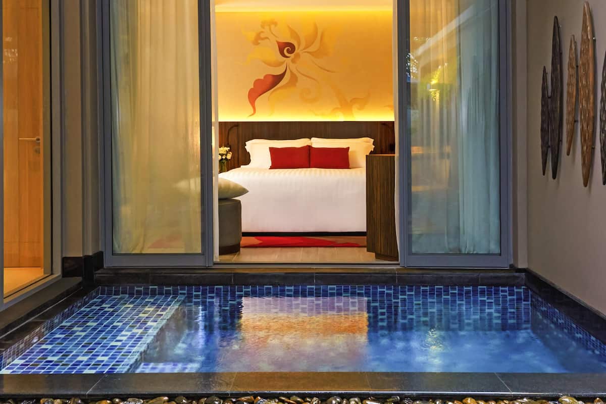 Una habitación de hotel moderna con una cama grande, un separador de vidrio y una pequeña zona de piscina.