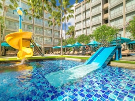 Una piscina alberghiera con uno scivolo acquatico, lettini e ombrelloni.