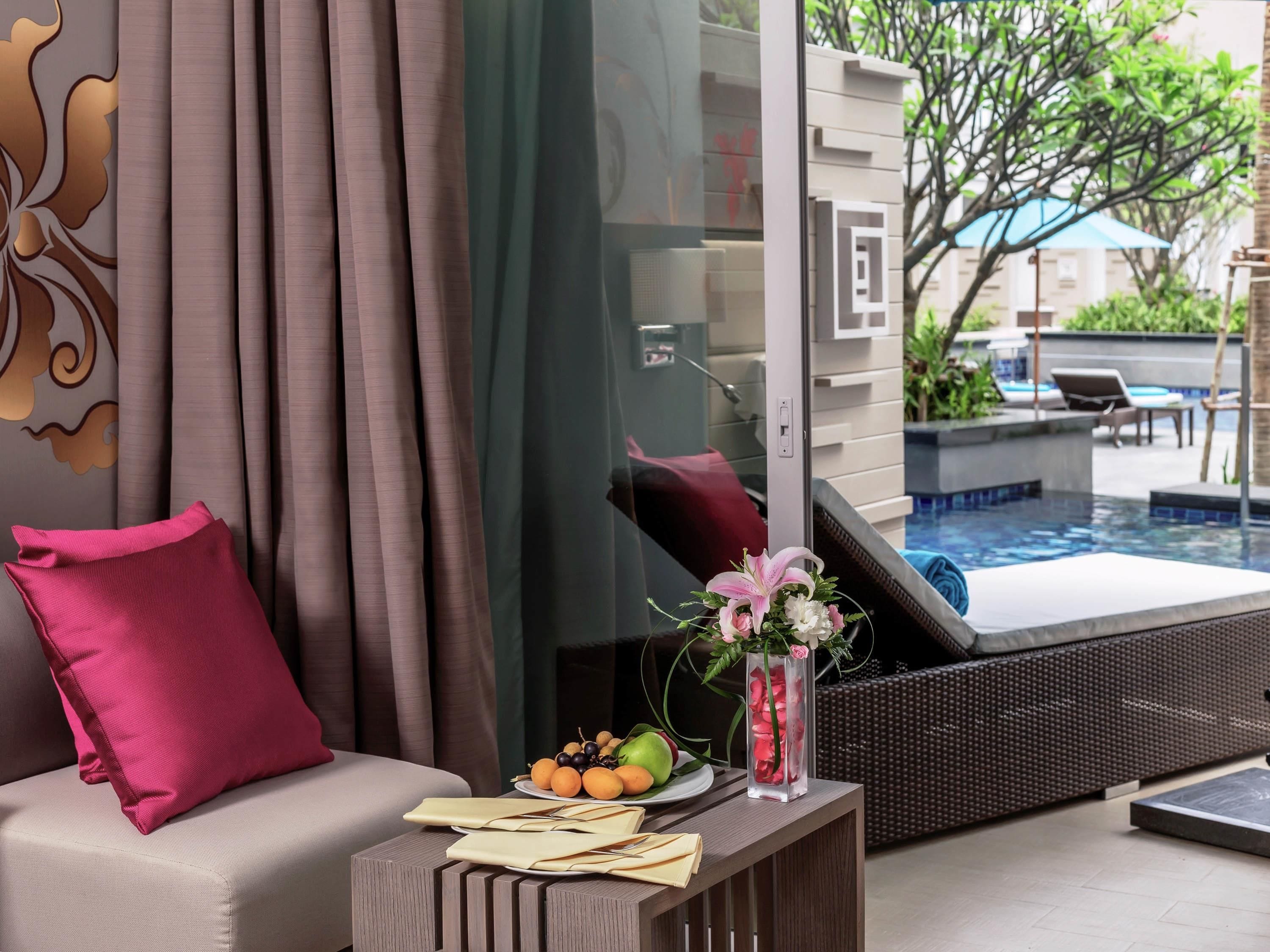 Ein modernes Zimmer mit einer Couch, einem kleinen Tisch mit Blumen und Blick auf ein Außenbecken.