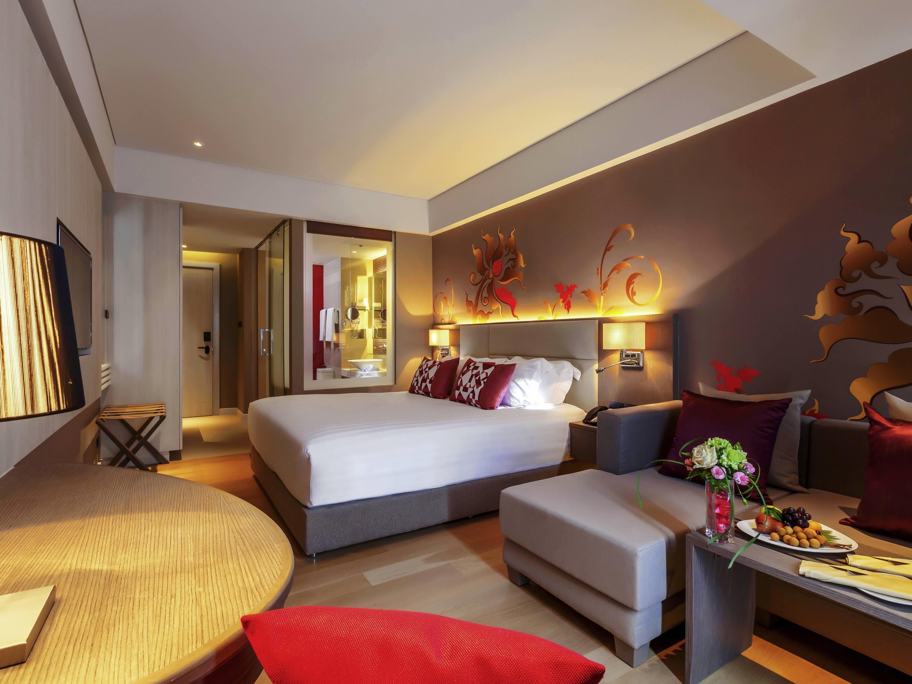 A modern hotel room with a large bed, a seating area with a round table, and a small kitchenette.