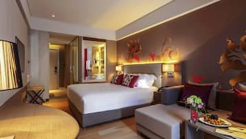 A modern hotel room with a large bed, a seating area with a round table, and a small kitchenette.