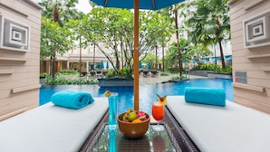 A poolside area with lounge chairs, a table with a fruit bowl, drinks, and a large umbrella.