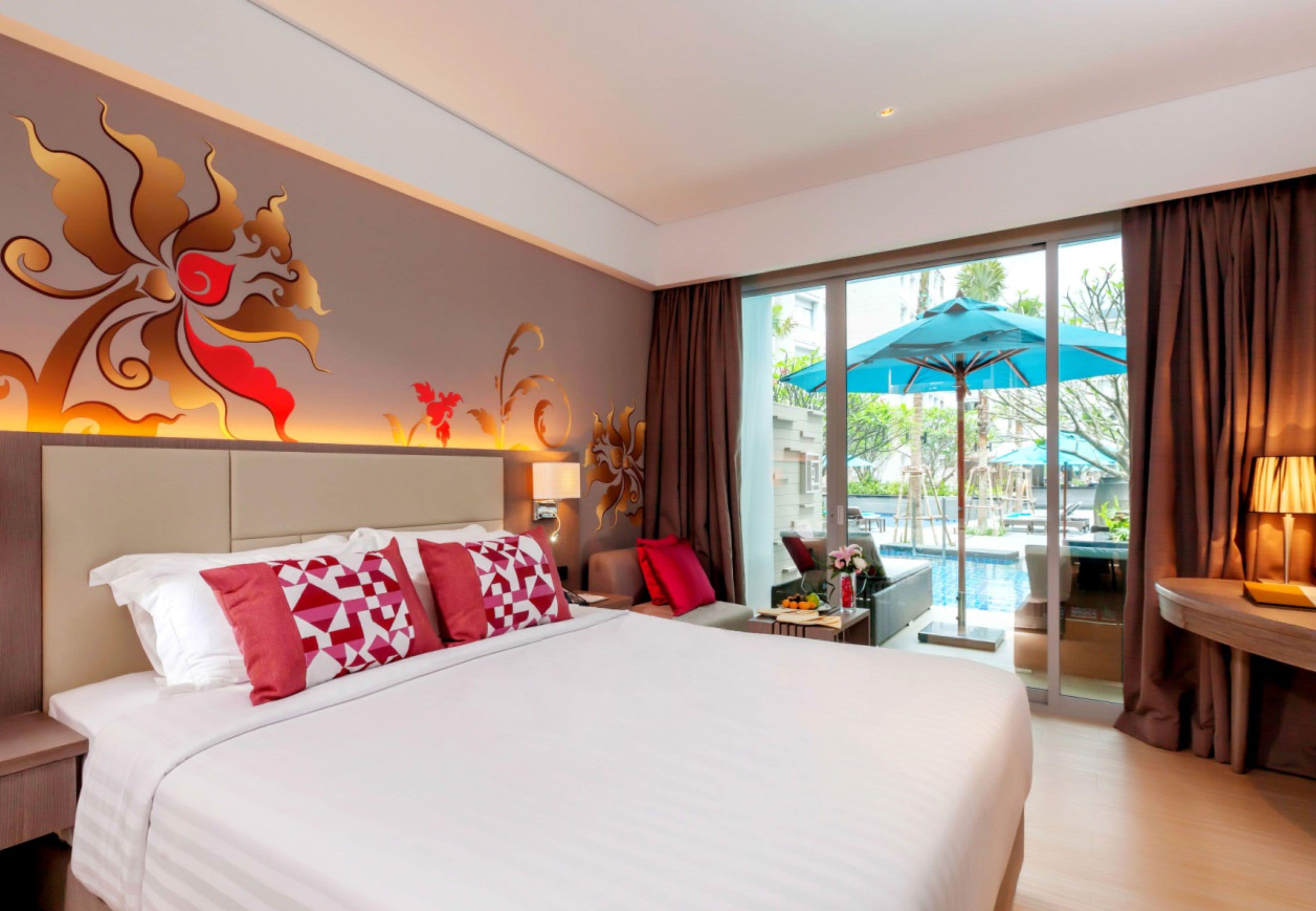 A hotel room with a large bed, a view of a swimming pool, and a decorative wall mural.