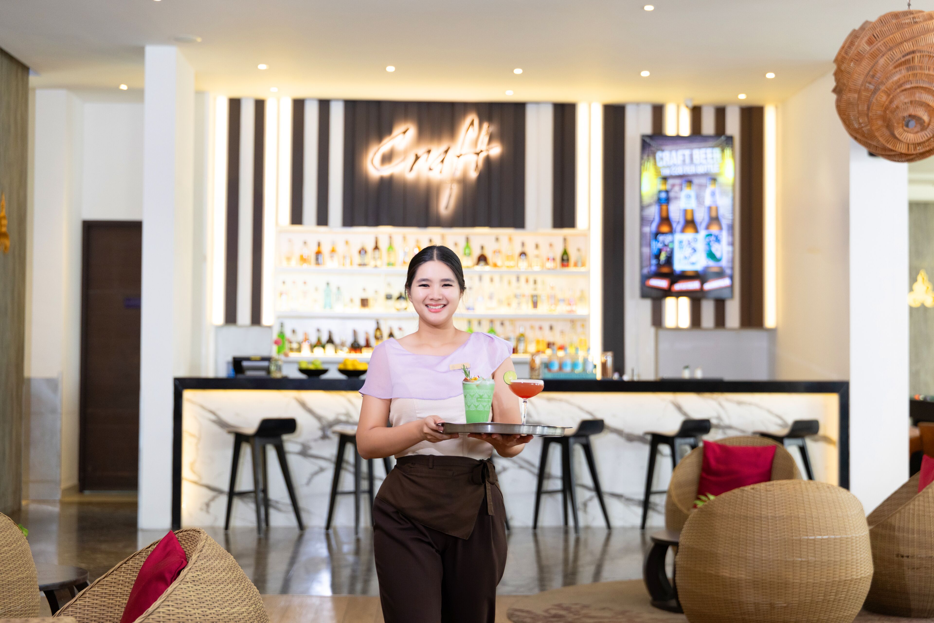 A bar area with a neon sign, a variety of bottles, and a television screen displaying a craft beer advertisement.