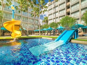Une piscine dâhĂŽtel avec un toboggan, des chaises longues et des parasols.