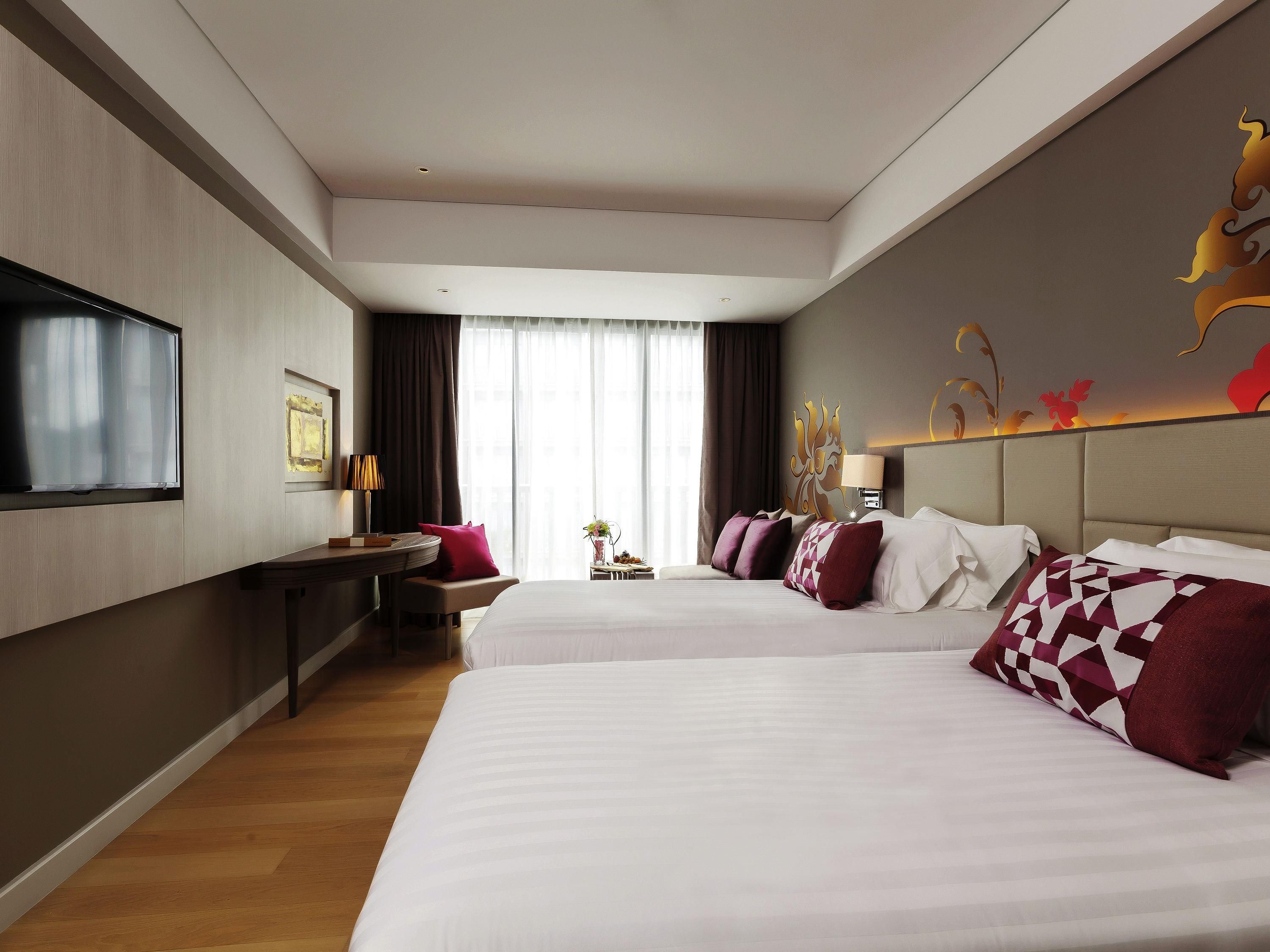 A hotel room with two beds, a desk, a TV, and a large window with curtains.