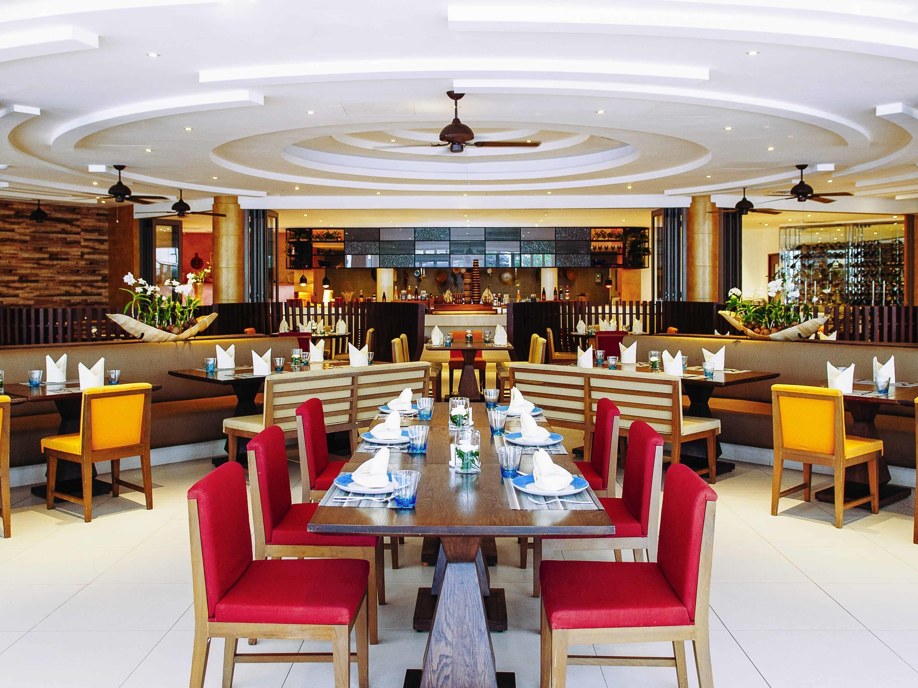 A spacious dining area with multiple tables and booths, a central bar, and a modern ceiling design.