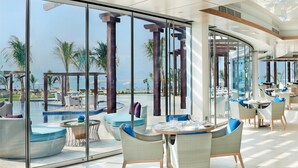 Un moderno vestíbulo de hotel con amplios ventanales, zona de piscina y mobiliario de exterior.