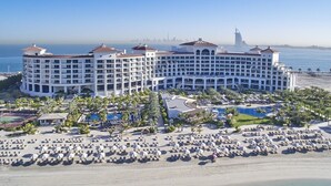 Un gran complejo turístico con varias edificaciones, una piscina y una zona de playa con sombrillas y sillas de descanso.