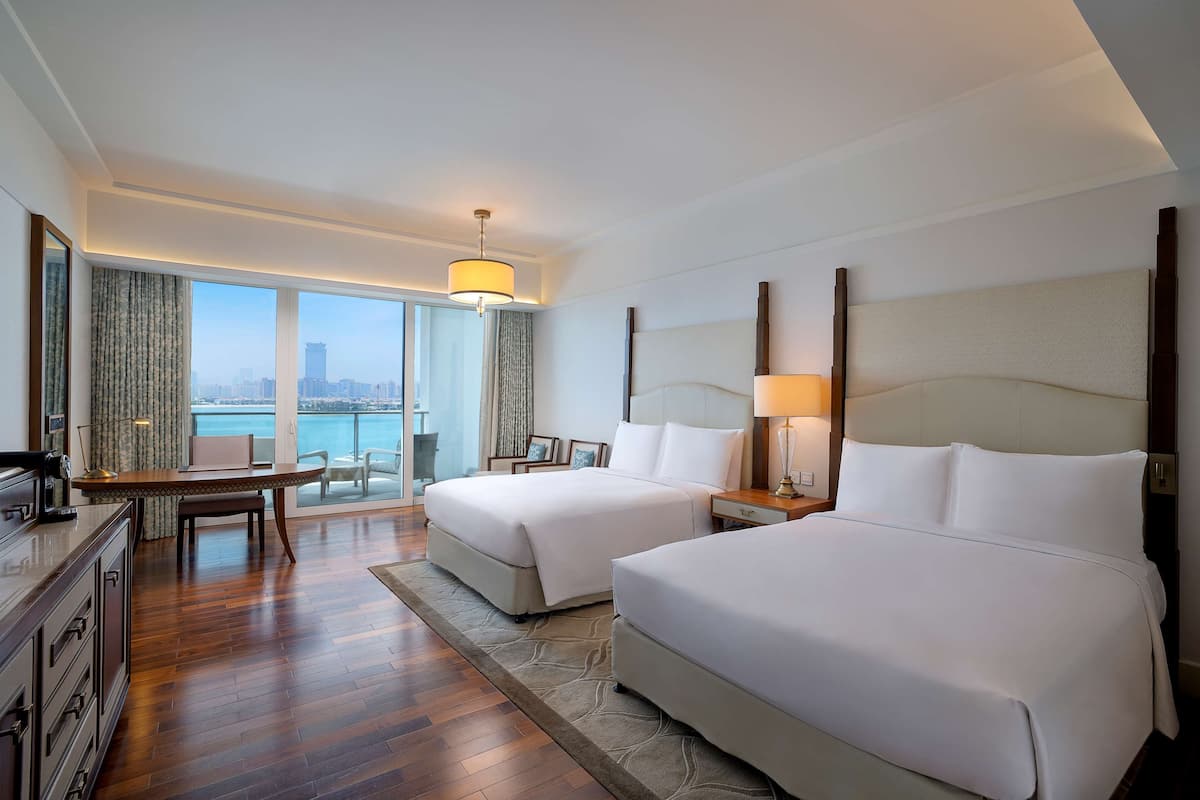 A hotel room with two beds, a desk, and a view of the city.