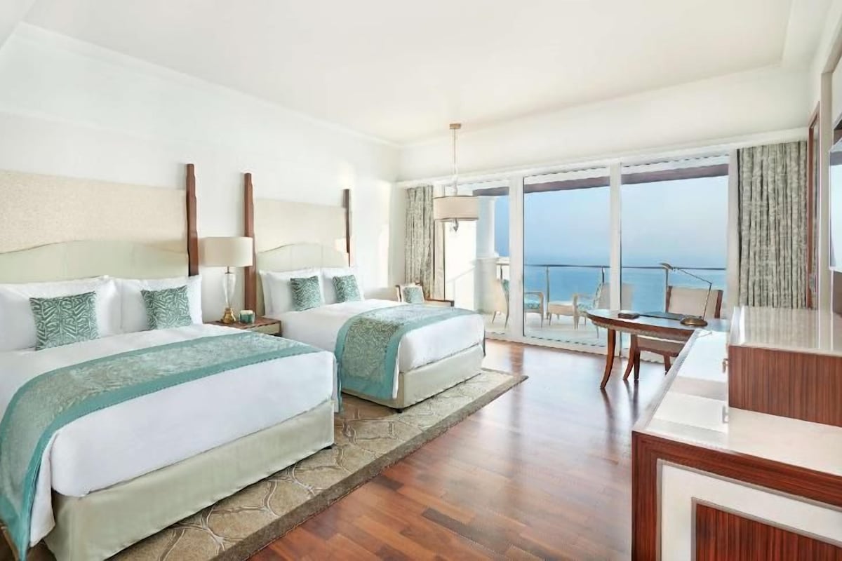 Habitación de hotel con dos camas, un balcón y vistas, un escritorio y una silla.
