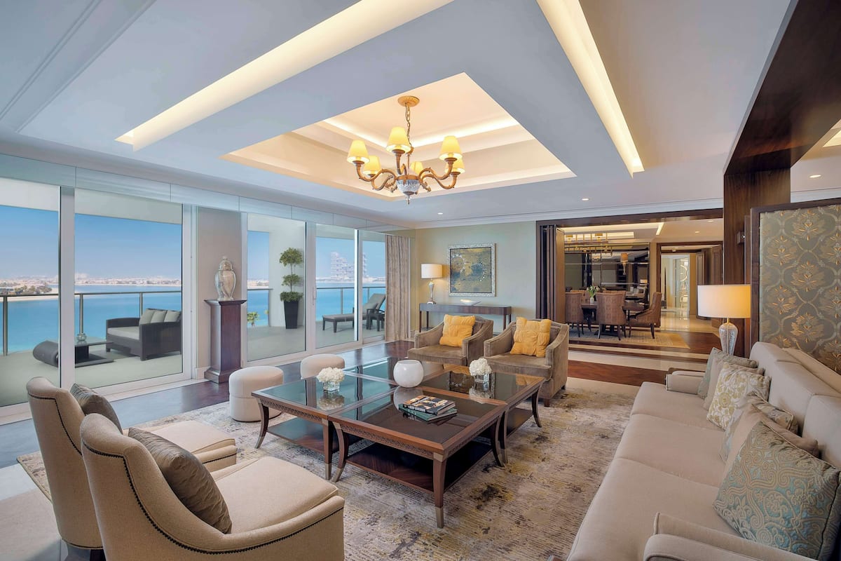 A spacious living room with a glass partition, a chandelier, and a view of the sea.